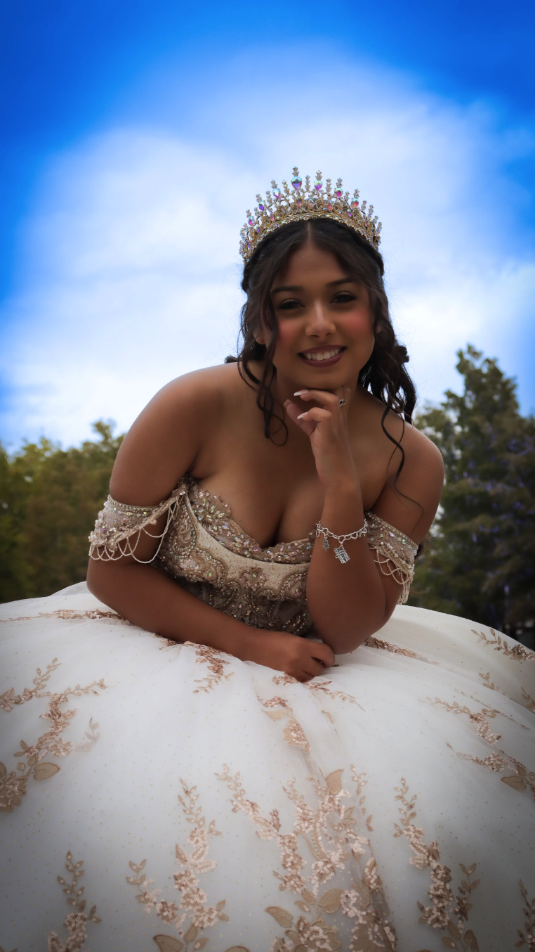 Quinceañera in beaded champagne gown with crystal crown against blue sky