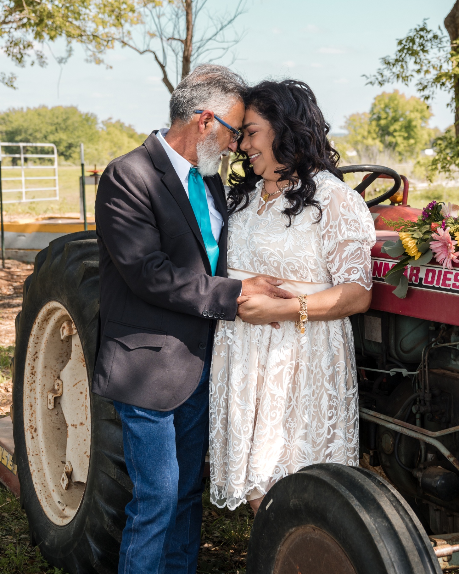 Couple foreheads together beside a vintage red tractor