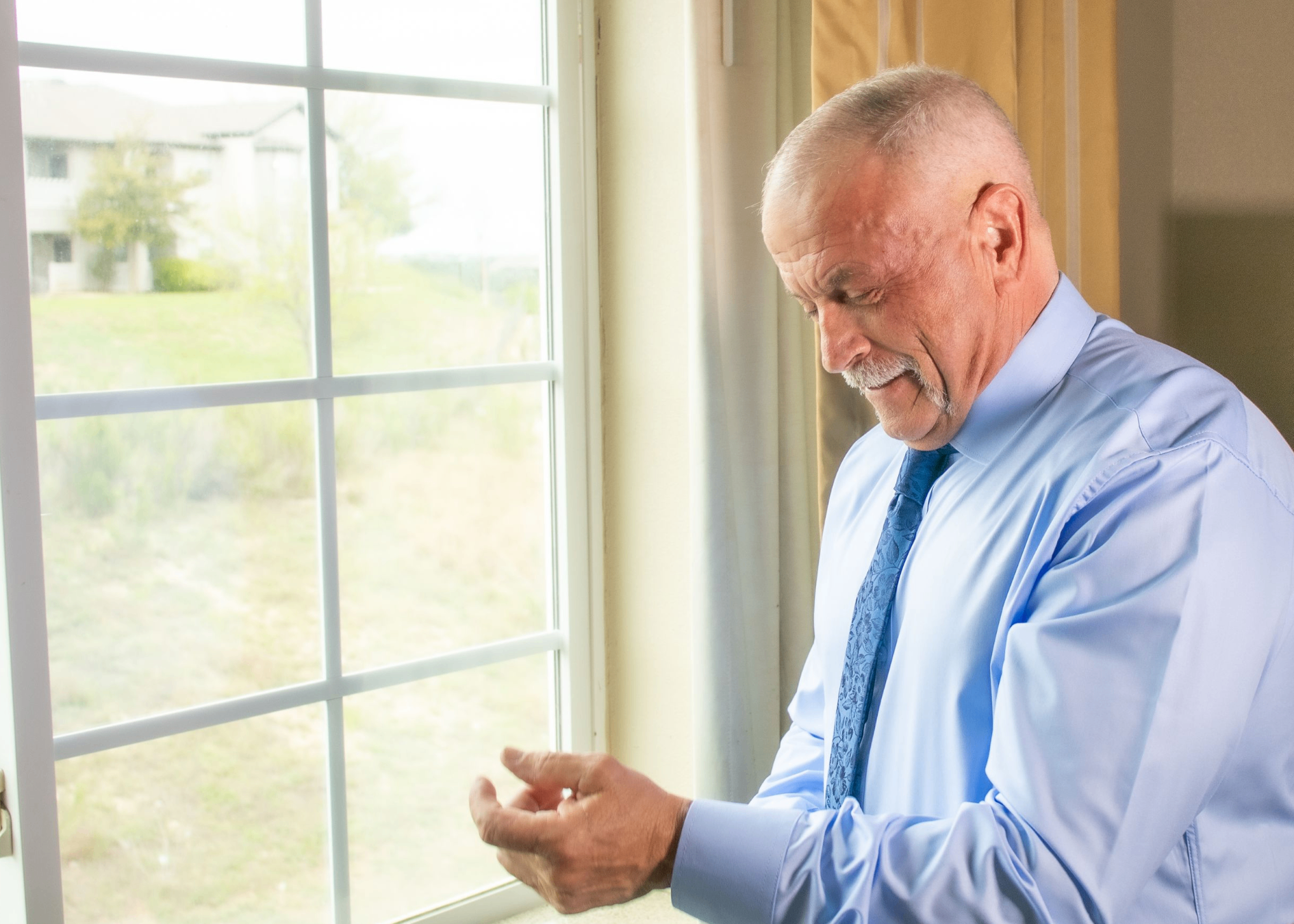 Groom fixing his cufflinks by the window in soft morning light