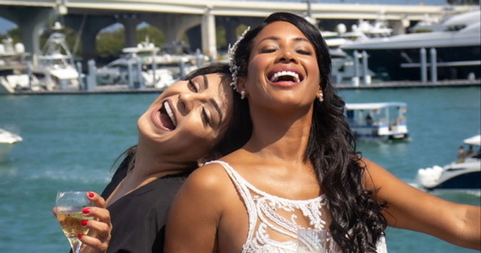 Bride laughing with her best friend, champagne in hand, by the marina