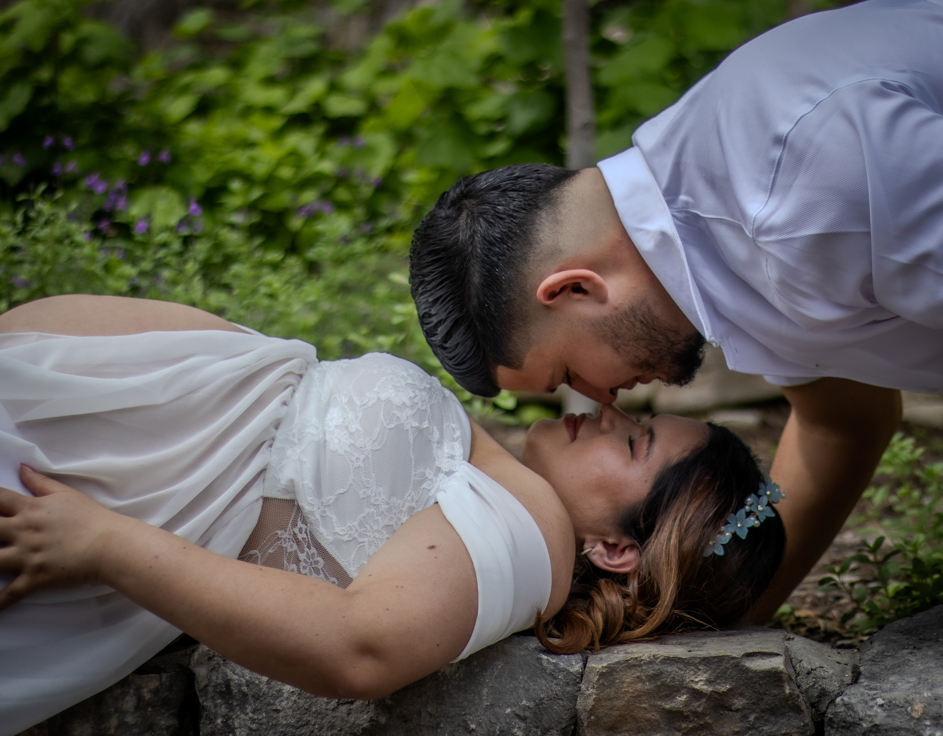 Couple kissing over a stone ledge, maternity shoot